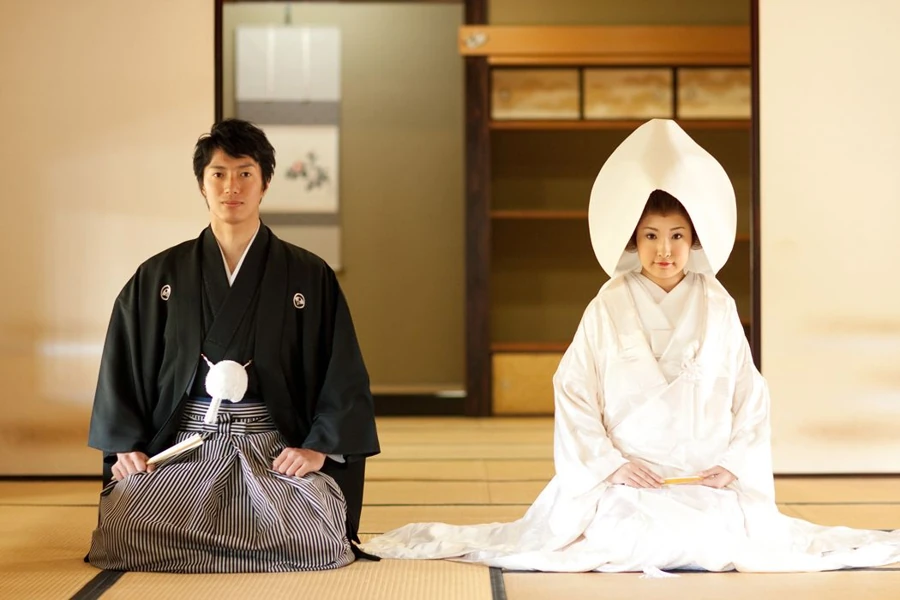 Shinto wedding couple seated together, the bride in a white shiromuku and wataboshi and the groom in a formal black kimono