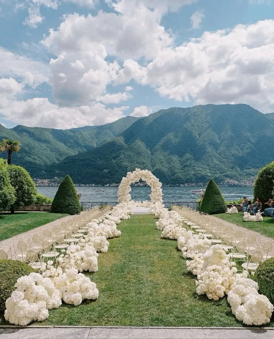 White floral wedding ceremony beside an Italian lake and mountains