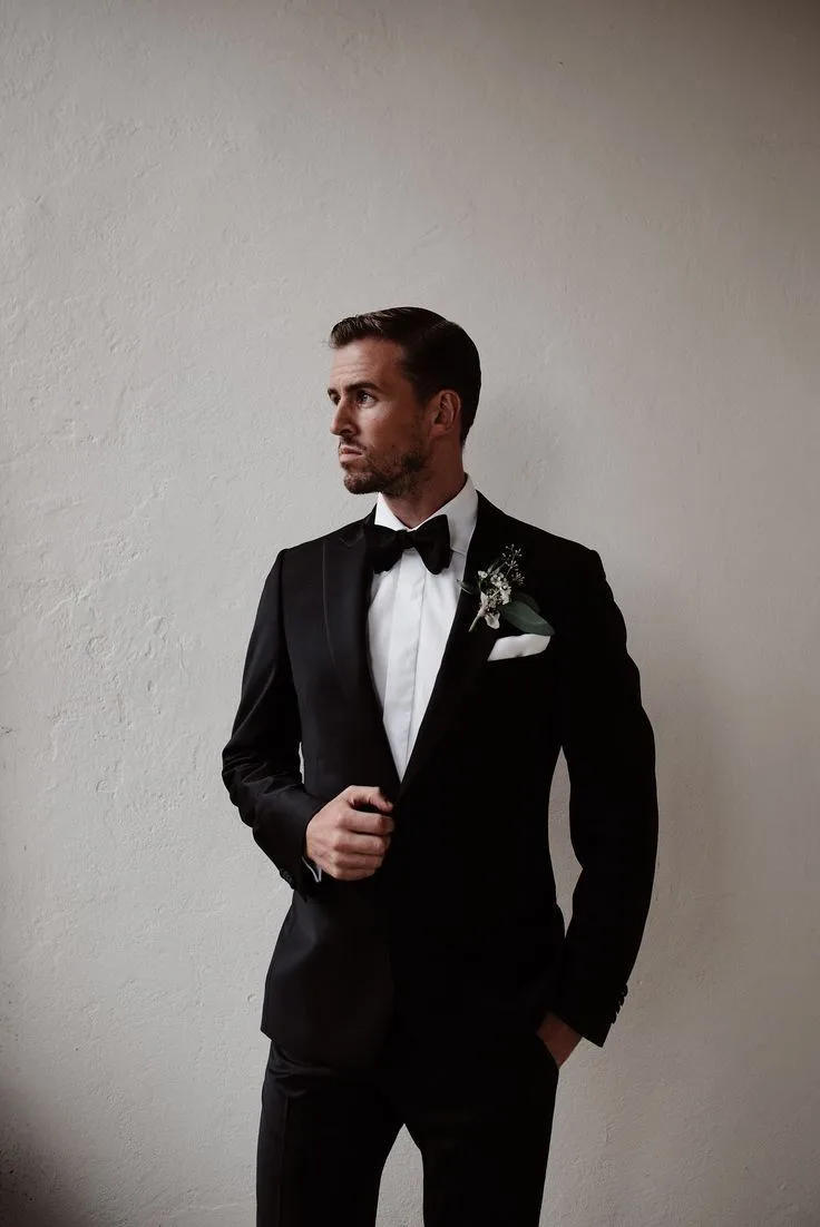 Groom photographed in a classic black tuxedo with a black bow tie