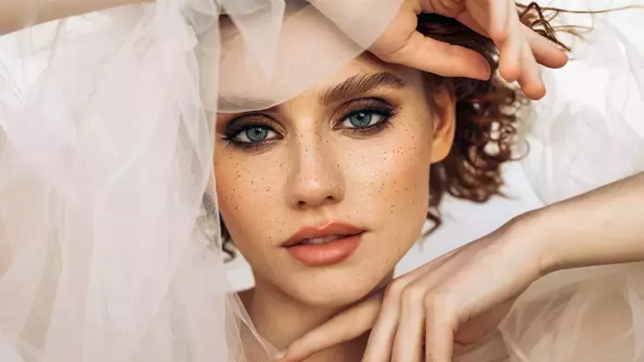Editorial bridal model framed by a veil with smoky eyes and glowing skin
