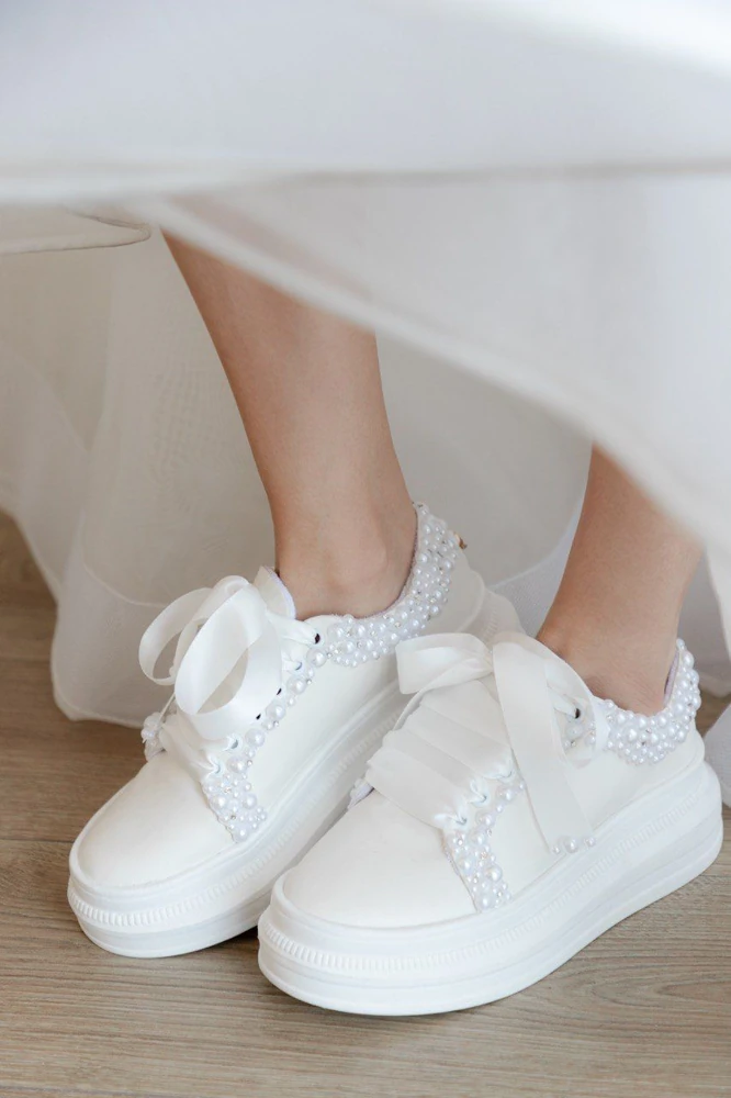 Bride wearing white pearl-embellished sneakers beneath her wedding gown